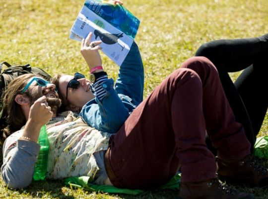 A Man And Woman Lying On The Grass Reading A Book