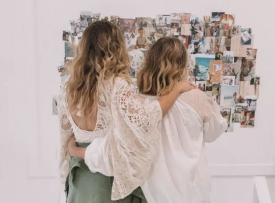 Two People Kissing In Front Of A Wall Of Photographs